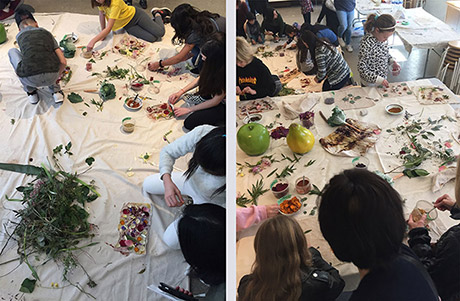 two images with about eight kids standing or sitting around large cotton fabric laid out on table and on floor indoors, sarrounded with leaves, flowers, and dried plant materials, making compositions on small peieces of fabric to get dye effects. 