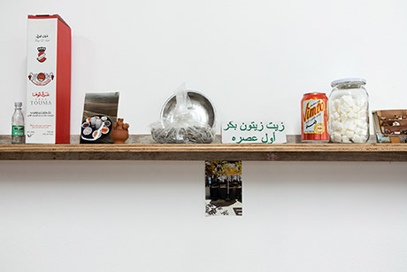 portion of the wall length shelf work holding arak, photographs, small clay pot, sundlower seeds, a pop can, cube sugar