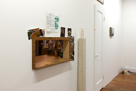 view of wood framed hole in the wall, allowing the food created in the back to be served to the gallery side. the wooden frame of the hole is adorned with photographs of foods taken by the artists