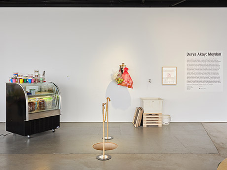 installation view with the a cafe display fridge full of food cooked by derya in forground