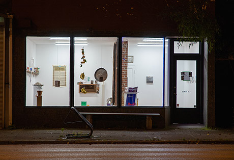 view of The Neighbour's Plate oh how it is visible form the street. A bright room with hanging fruits and pans by the front windows, and a redbull fridge is visible in the foreground. 