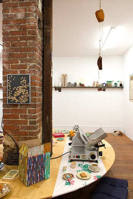 view of the table in the center of the room, the back of the table holds an industrial meat slicer and hand painted cardboard box